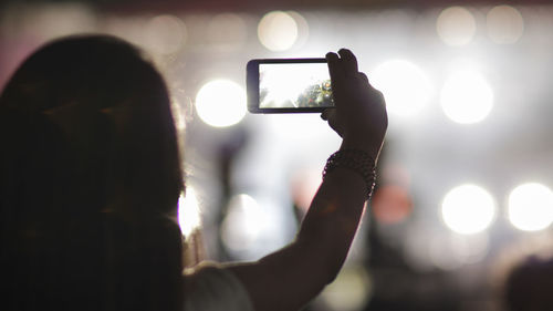 Rear view of mid adult woman photographing through smart phone in illuminated street at night