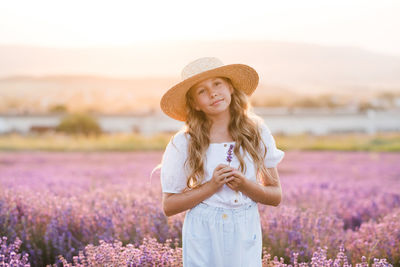 Cute child girl 8-9 year old with long blonde hair wear straw hat in bloom lavender field outdoor