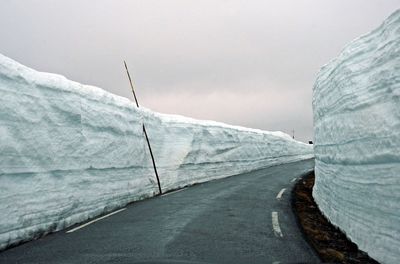 Snow covered road by mountain against sky