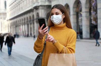 Young woman wearing mask using mobile phone outdoors