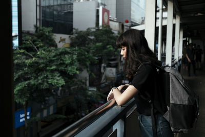 Side view of young woman standing by railing in balcony