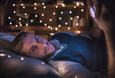 Portrait of young man using mobile phone while lying on bed at home