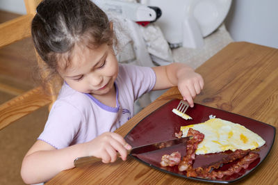 Young girl eating eggs and bacon with knife and fork for the first time