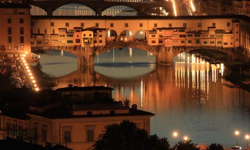Illuminated bridge over river in city at sunset