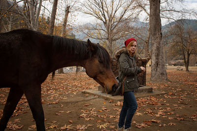 Portrait of woman touching horse amidst bare trees on field during autumn