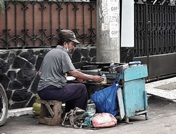 Side view of man sitting on garbage against building