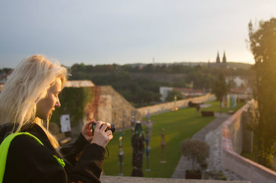 Side view portrait of woman holding camera against sky