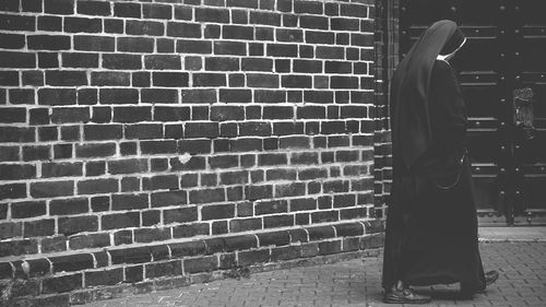 Rear view of woman standing against brick wall