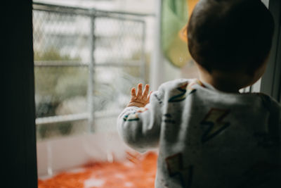 Rear view of boy standing by glass window