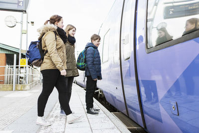 Full length of school friends waiting for train doors to open