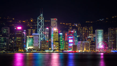 Illuminated buildings by river against sky at night