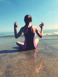 Rear view of girl gesturing while sitting at beach against sky