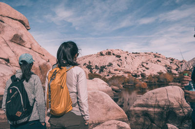 Rear view of woman standing on rock against sky