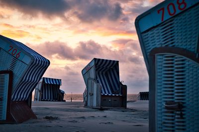 Hooded beach chairs against sky during sunset