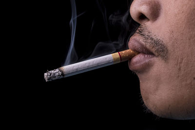 Cropped image of man smoking cigarette against black background