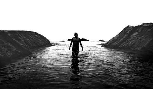 Rear view of man walking on beach against clear sky