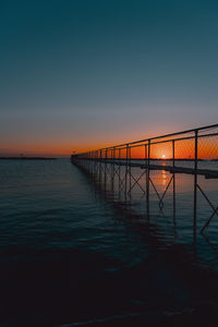 Pier over sea against clear sky at sunset
