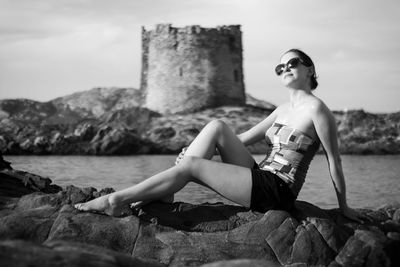 Woman sitting on rock against sky