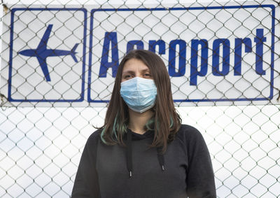Low angle view of woman wearing mask standing against fence