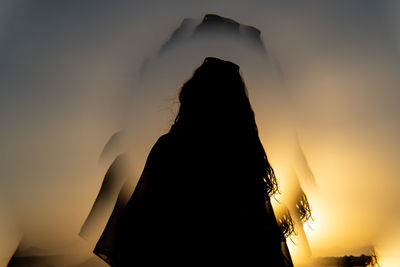 Rear view of woman standing against sky during sunset