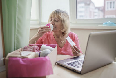 Senior woman holding playing card sitting by laptop at home