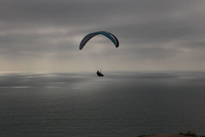 Silhouette person paragliding over sea against sky