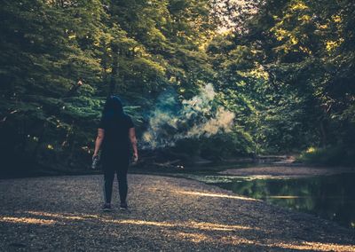 Rear view of woman standing on road by trees