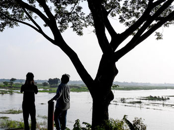 Rear view of people standing by lake against sky