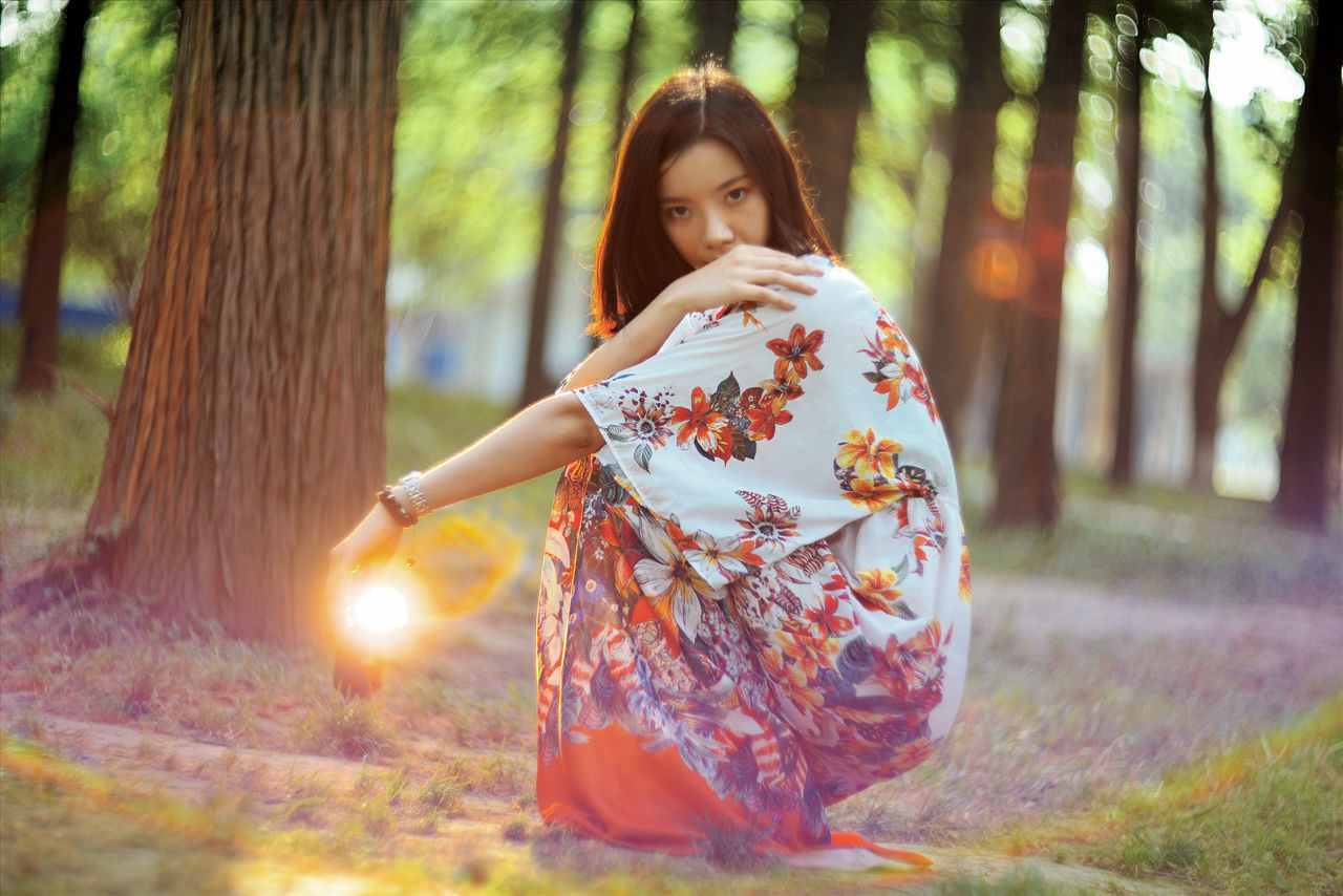 tree, focus on foreground, lifestyles, leisure activity, front view, casual clothing, standing, person, forest, sunlight, outdoors, day, childhood, lens flare, park - man made space, looking at camera, full length, portrait