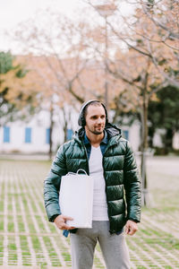 Mid adult man holding bag looking away while standing outdoors