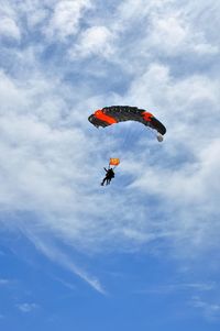 Low angle view of people paragliding against sky