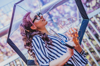 Side view of smiling young woman holding light bulb under umbrella