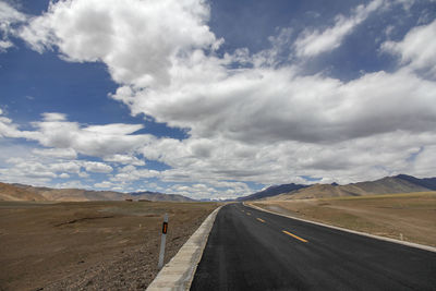 A flat, newly built wide asphalt road leads to the beautiful mountains in the distance
