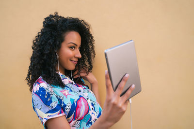 Young woman using phone while standing on wall