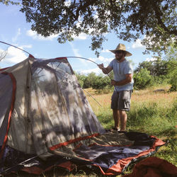 Man wearing hat while putting tent on grassy field