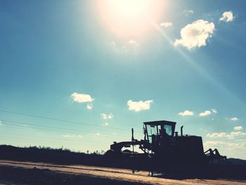 Silhouette earth mover on field against sky during sunny day