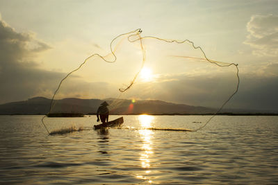 Silhouette of man fishing in sea during sunset