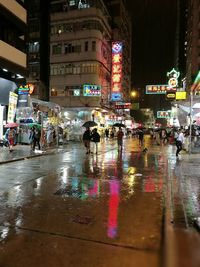 People walking on wet road in city at night