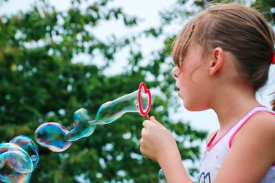 Side view of girl blowing bubbles at yard