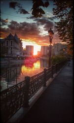 City street by river against sky during sunset