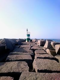 Lighthouse by sea against buildings against clear blue sky