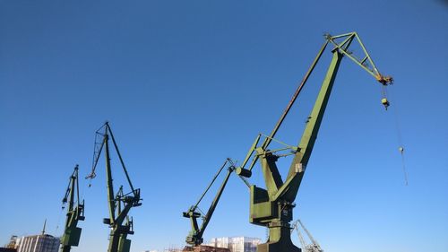 Low angle view of cranes against clear blue sky