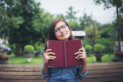 Thoughtful young woman looking away while holding book on park bench