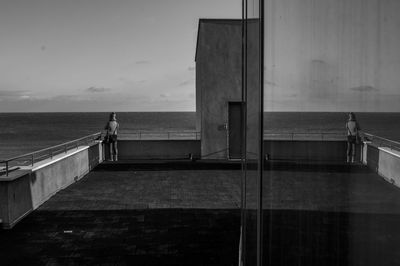 Reflection of woman standing by railing while looking at sea against sky