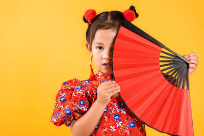 Young woman holding umbrella against yellow background