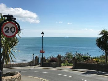 Road sign by sea against sky