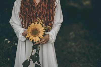 Midsection of woman holding white flower in field