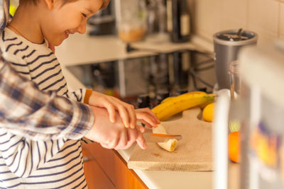 Midsection of mother teaching son to cut banana at home