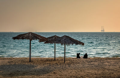 People on beach against clear sky during sunset