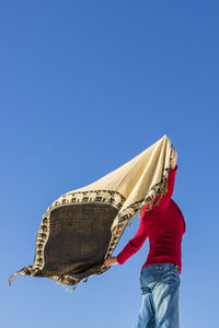 Low angle view of person holding umbrella against clear blue sky